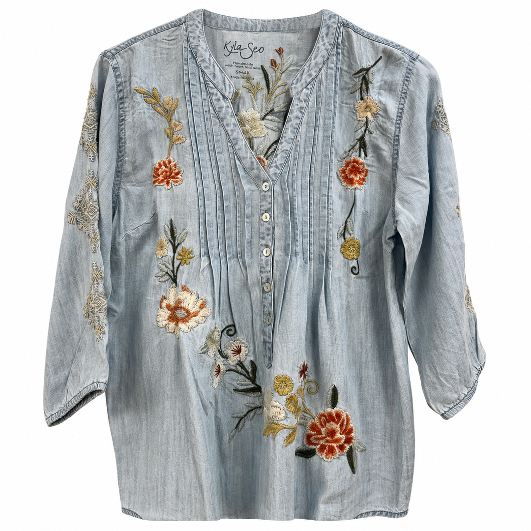 A light blue chambray button-up blouse by St. Joe's with floral embroidery in orange, yellow, and green, shown flat against a white background.